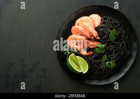 Schwarze Spaghetti-Pasta-Garnelen auf schwarzer Platte auf dunklem Betontischhintergrund. Tintenfischpasta mit Garnelen. Nudelgerichte mit Meeresfrüchten. Ansicht von oben auf der Lasche des schwarzen Steins Stockfoto