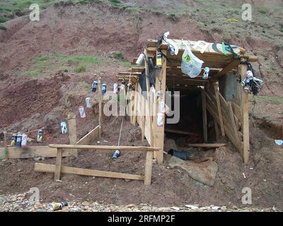 Eine Hütte aus Treibholz am Fuße einer instabilen Klippe auf der Isle of Wight. Dekoriert mit verschiedenen Getränkedosen. Stockfoto