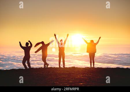 Eine Gruppe glücklicher Touristen hat Spaß und tanzt bei Sonnenaufgang auf dem Berggipfel über den Wolken Stockfoto