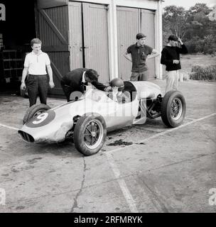 1962, historisch, ein junger Fahrer sitzt in einem Einsitzer-Cooper-Auto vor den Schuppen der Rennfahrerschule am Finmere Aerodrome, Bucks, England, Großbritannien, Stockfoto