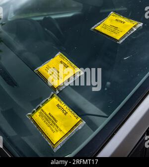 Mehrere Parkscheine oder Strafgebühren auf der Windschutzscheibe eines auf der Straße geparkten Autos Stockfoto