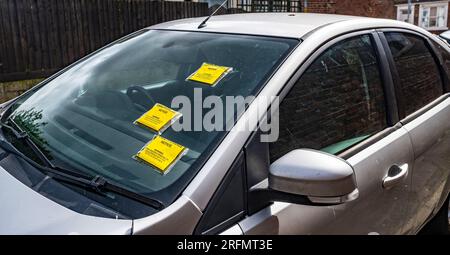 Mehrere Parkscheine oder Strafgebühren auf der Windschutzscheibe eines auf der Straße geparkten Autos Stockfoto