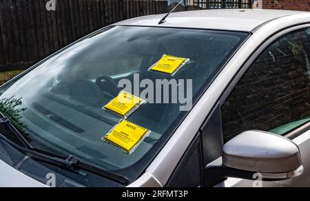 Mehrere Parkscheine oder Strafgebühren auf der Windschutzscheibe eines auf der Straße geparkten Autos Stockfoto