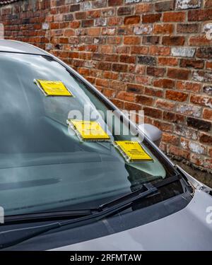 Mehrere Parkscheine oder Strafgebühren auf der Windschutzscheibe eines auf der Straße geparkten Autos Stockfoto