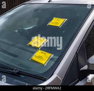 Mehrere Parkscheine oder Strafgebühren auf der Windschutzscheibe eines auf der Straße geparkten Autos Stockfoto