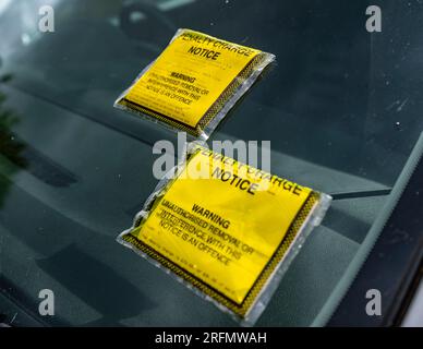 Mehrere Parkscheine oder Strafgebühren auf der Windschutzscheibe eines auf der Straße geparkten Autos Stockfoto