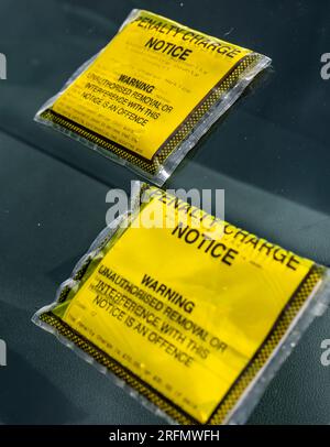 Mehrere Parkscheine oder Strafgebühren auf der Windschutzscheibe eines auf der Straße geparkten Autos Stockfoto
