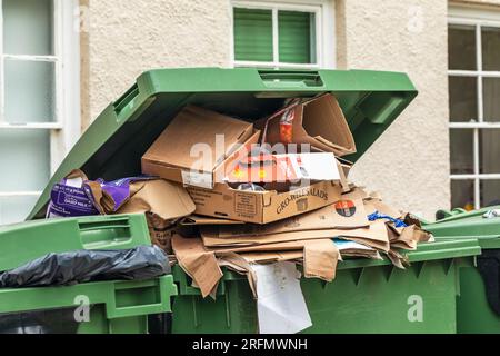 Überlaufender, gefüllter, grüner Recyclingbehälter aus Pappe wartet auf die Abholung, City of Wells, Somerset, England, Großbritannien Stockfoto