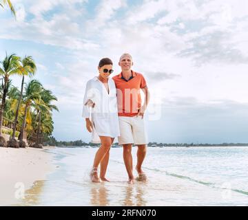 Ein Paar, das sich umarmt, während man auf einem exotischen Sandstrand spaziert. Sie machen einen Abendspaziergang an der Küste von Trou-aux-Biches auf Mauritius Island. Verwandte Stockfoto