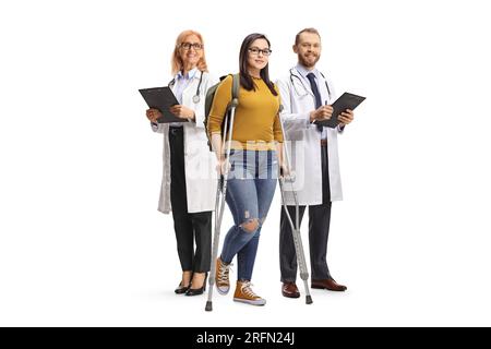 Studentin mit Krücken vor Ärzten isoliert auf weißem Hintergrund Stockfoto