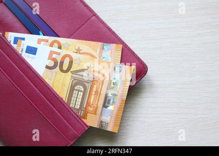 50-Euro-Scheine in einer Lederbörse. Rote Geldbörse, Handtasche. Holzhintergrund. Banknoten. Geld in bar Stockfoto
