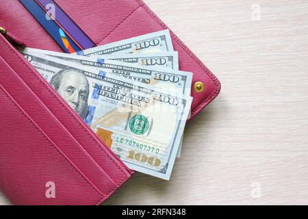 100-Dollar-Scheine in einer Lederbörse. Rote Geldbörse, Handtasche. Holzhintergrund. Banknoten. Geld in bar. Notizenstapel. Ein Fan von Rechnungen. USD Stockfoto