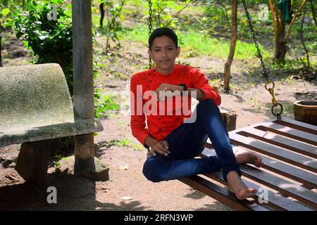 Ein Indianerjunge in rotem Hemd und blauer Jeans sitzt in einer Eisensauge. Gartenhintergrund Stockfoto