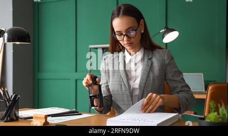 Weibliche Notaröffentlichkeit, die Siegel an Dokumenten im Büro anschließt Stockfoto