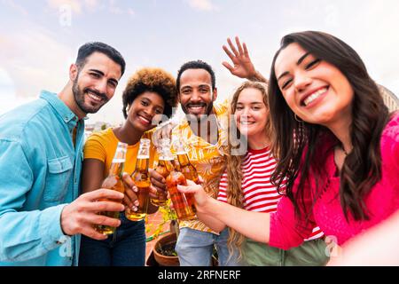 Eine multiethnische Gruppe glücklicher junger Freunde veranstaltet zu Hause eine Barbecue-Dinner-Party auf dem Dach - multiethnische, fröhliche junge Erwachsene, die Spaß und Bindung haben Stockfoto