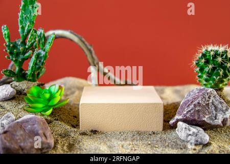 Beigefarbenes Podium mit Kakteen und Treibholz für die Produktpräsentation. Nachahmung der Wüste, roter Hintergrund. Stockfoto