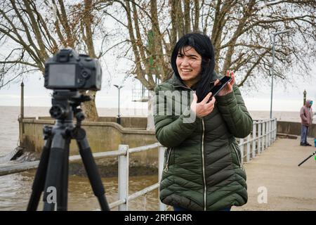 Eine junge venezolanische Latina-Frau, eine Reisende-Vloggerin mit ihrer Kamera, die Inhalte für soziale Netzwerke erstellt, ihr Handy im Video verwendet und den Por besucht Stockfoto
