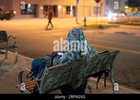 Ein Mann, der auf der Straße lebt, schaut auf ein Handy, während er in der Innenstadt von Austin an einer kühlen Januarnacht im Zentrum von Texas versucht, sich warm zu halten. ©Bob Daemmrich Stockfoto