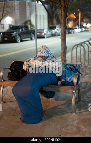 Ein Mann, der auf der Straße lebt, schaut auf ein Handy, während er in der Innenstadt von Austin an einer kühlen Januarnacht im Zentrum von Texas versucht, sich warm zu halten. ©Bob Daemmrich Stockfoto