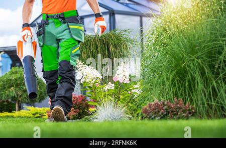 Professioneller Gartenarbeiter, der auf dem Hinterhof mit einem Gebläse in der Hand spaziert Stockfoto