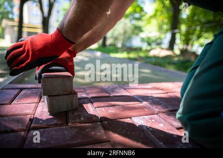 Ein qualifizierter Bauarbeiter legt rote Pflastersteine auf einen Bürgersteig. Stockfoto