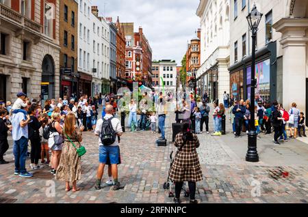 Ein Straßenzauber schluckt einen Ballon, während er im Covent Garden im Londoner West End WC2 eine begeisterte, würdige Menge vorführt und unterhält Stockfoto