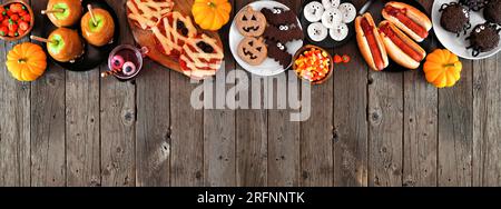 Halloween-Party-Essen am oberen Rand mit rustikalem Holzbanner-Hintergrund und Kopierbereich. Über der Ansicht. Gruselige Mumienpizzen, Finger-Hotdogs, Karamell-Äpfel Stockfoto