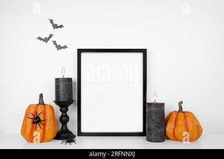 Halloween-Modell. Schwarzer Rahmen auf weißem Regal mit Kürbis-Dekor und schwarzen Kerzen. Porträtrahmen an einer weißen Wand mit Fledermäusen. Speicherplatz kopieren. Stockfoto