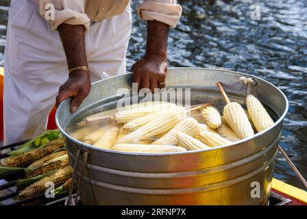 Nahaufnahme der Hände eines Straßenverkäufers, der eine große, mit gekochtem Mais gefüllte Wanne sicher hält, ein beliebter Snack in Xochimilco, Mexiko. Stockfoto