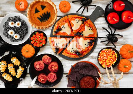 Lustige Halloween-Dinner-Party-Tischszene mit weißem Holzhintergrund. Ansicht von oben nach unten. Geisterpizza, Augapfel-Spaghetti, Jack o Laternen Kürbiskuchen, Süßigkeiten Stockfoto