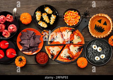 Lustige Halloween-Party-Tischszene mit dunklem Holzhintergrund. Draufsicht. Pizza, Jack o Laterne Kürbiskuchen, Süßigkeiten Äpfel, Augapfel Spaghetti, Snack Stockfoto