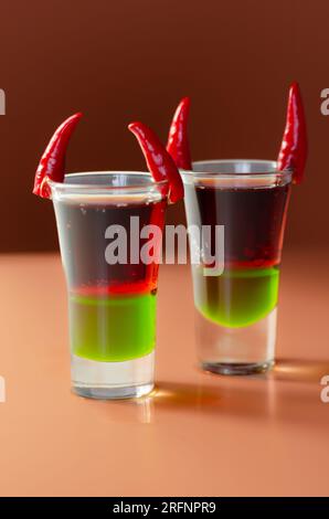 Mehrschichtiger Getränkeschuss zubereitet mit Wodka, grünem Likör, Grenadine und Zitronensaft dekoriert mit Vogelaugen-Chillies in Form von Hörnern, Teufelsschuss Stockfoto