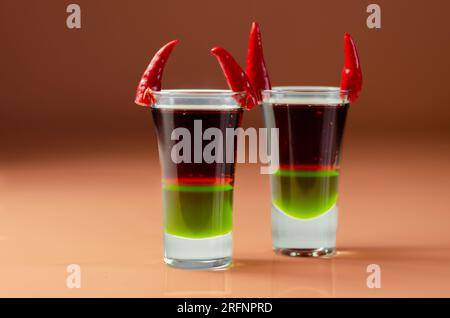 Mehrschichtiger Getränkeschuss zubereitet mit Wodka, grünem Likör, Grenadine und Zitronensaft dekoriert mit Vogelaugen-Chillies in Form von Hörnern, Teufelsschuss Stockfoto