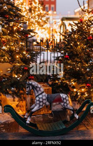 Goldener Weihnachtsabend und Retro-Kinderpferd Karussell in der Nähe des Weihnachtsbaums. Vertikale magische Postkarte Stockfoto