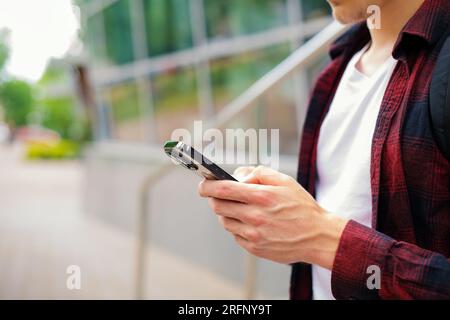 Unbekannter junger Geschäftsmann in rotem Hemd mit modernem Smartphone in den Händen im Freien, 5 g Internet, Textnachrichten, Videoanrufe Stockfoto