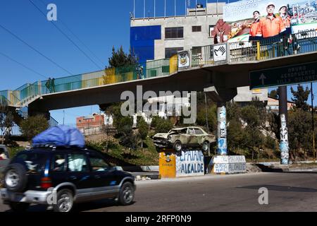 Ein Auto fährt an einem Unfallauto vorbei, das auf einem Sockel mitten auf der Autobahn steht, und warnt die Fahrer, nicht zu trinken, fahren und vorsichtig fahren, La Ceja, El Alto, Bolivien Stockfoto