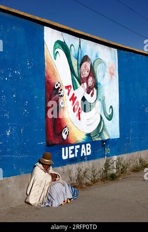 Ältere Aymara-Frau, die auf dem Bürgersteig neben dem Wandgemälde sitzt, Teil einer Kampagne zur Verringerung von häuslicher Misshandlung und Gewalt gegen Frauen, El Alto, Bolivien Stockfoto