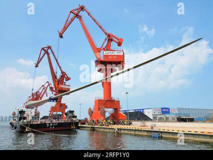 YANTAI, CHINA - 4. AUGUST 2023 - Ein Kran hebt B1260A supergroße Offshore-Windturbinenblätter von einem Frachtschiff im Penglai Port Area von Yantai Po Stockfoto