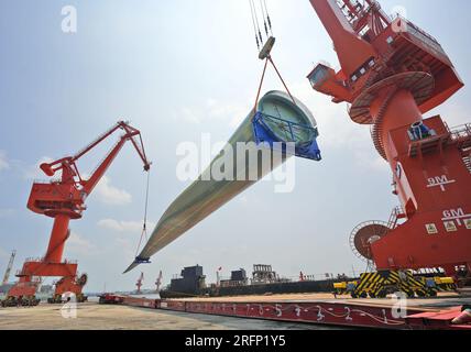 YANTAI, CHINA - 4. AUGUST 2023 - Ein Kran hebt B1260A supergroße Offshore-Windturbinenblätter von einem Frachtschiff im Penglai Port Area von Yantai Po Stockfoto