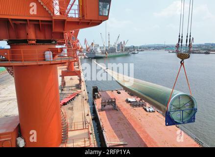 YANTAI, CHINA - 4. AUGUST 2023 - Ein Kran hebt B1260A supergroße Offshore-Windturbinenblätter von einem Frachtschiff im Penglai Port Area von Yantai Po Stockfoto