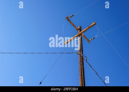 Ein alter elektrischer Holzmast mit Drähten und einem klaren blauen Himmel in Joshua Tree, Kalifornien. Stockfoto