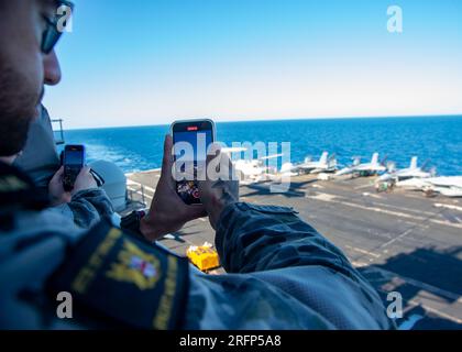 INDISCHER OZEAN (4. August 2023) Royal Australian Navy (RAN) Matrosen, die der RANNTEN Fregatte HMAS Perth (FFG 157) zugeteilt sind, fotografieren eine E-2D Hawkeye, die an der Tigerschwanzschwanzflosse der Airborne Early Warning Squadron (VAW) 125 befestigt ist, während sie auf dem Flugdeck der USA landet Der einzige Flugzeugträger der Navy, USS Ronald Reagan (CVN 76), im Indischen Ozean, am 4. August 2023. Ronald Reagan, das Flaggschiff der Carrier Strike Group 5, stellt eine kampfbereite Truppe bereit, die die Vereinigten Staaten schützt und verteidigt und Bündnisse, Partnerschaften und kollektive maritime Interessen im Indo-Pazifik unterstützt Stockfoto