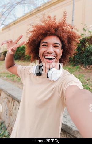 Vertikales Porträt eines glücklichen afroamerikanischen Kerls mit Afrohaar, der ein Selfie macht. Ein Teenager, der Spaß hat und lacht. Ein fröhlicher Mann mit einem zahnigen Lächeln, der einen Videoanruf hat. Erfolgreicher Universitätsstudent. Hochwertiges Foto Stockfoto