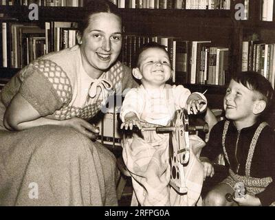 Deutsche Frau mit ihren beiden Kindern vor einem Bücherregal. Die jüngste, ein Mädchen, sitzt auf einem Schaukelpferd. Das Foto wurde um 1958 Uhr gemacht Stockfoto