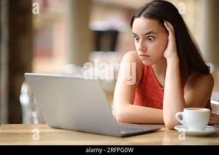 Schockierte Frau, die sich Notebook-Inhalte auf einer Bar-Terrasse ansieht Stockfoto