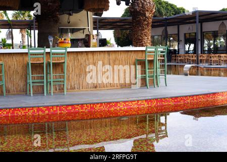 Tropic Bar am Pool an einem Sommertag mit Palmen im Hintergrund. Reflexion über Wasser und Stühle. Stockfoto