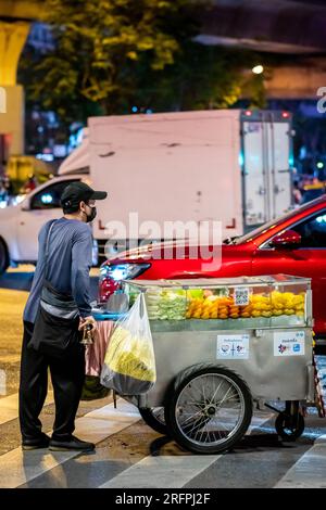 Ein thailändischer Obstverkäufer macht sich auf den Weg entlang der Silom Road In der geschäftigen Innenstadt von Silom, Bangkok City, Thailand. Stockfoto