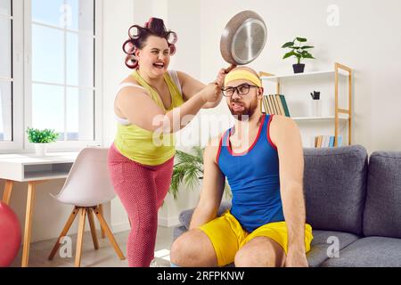 Lustige, verrückte Hausfrau, die Spaß hat und ihren Mann mit einer Bratpfanne auf den Kopf schlägt Stockfoto