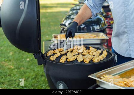 Ein Mann grillt während einer Grillparty im Garten Hühnchen auf Spießen Stockfoto