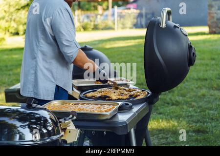 Ein Mann kocht im Sommer während einer Barbecue-Party Hühnerfleisch auf Spießen auf einem Grill im Garten Stockfoto